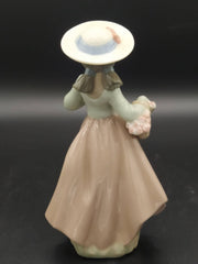 Vista trasera de la figura de porcelana Nao Lladó, mostrando detalles del vestido y sombrero de la niña con cesta de flores.