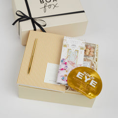 BOXFOX Creme Gift box containing Notem Gold Stripe notebook, BOXFOX Gold Bullet Pen, Compartes Cake & Sprinkles White Chocolate Bar, Sugarfina Birthday Cake Cookie Bites, Voluspa Bergamot Macaron Candle and Vitamasque Gold Eye Mask.
